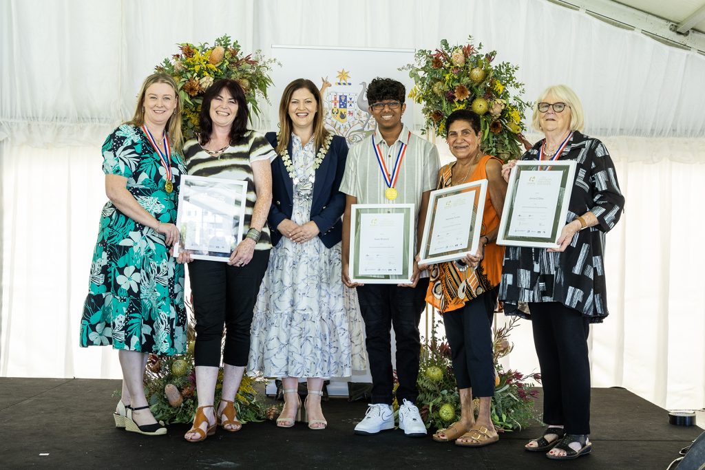 six people on stage holding certificates and smiling to camera