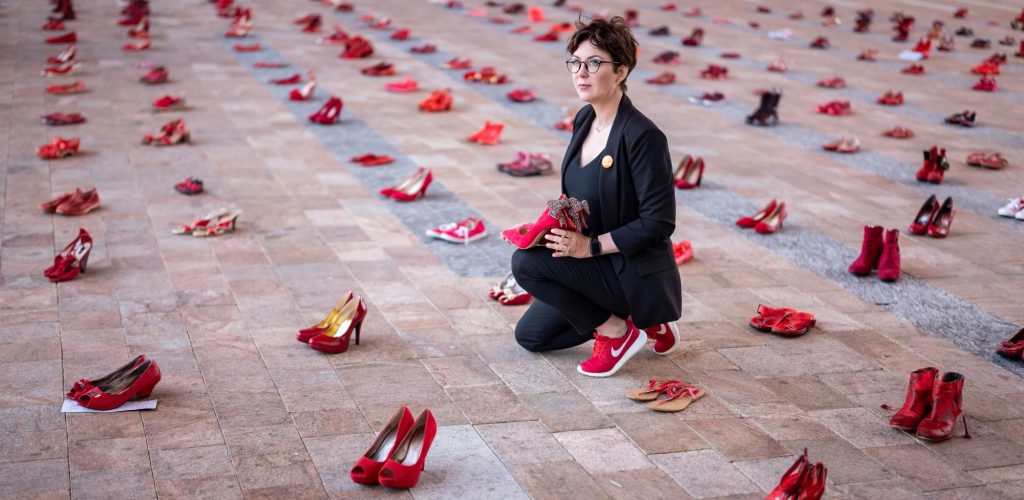 woman kneeling on ground surrounded by red shoes