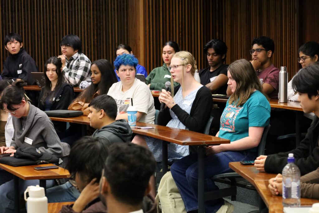 student speaking into a microphone with other students sitting around them