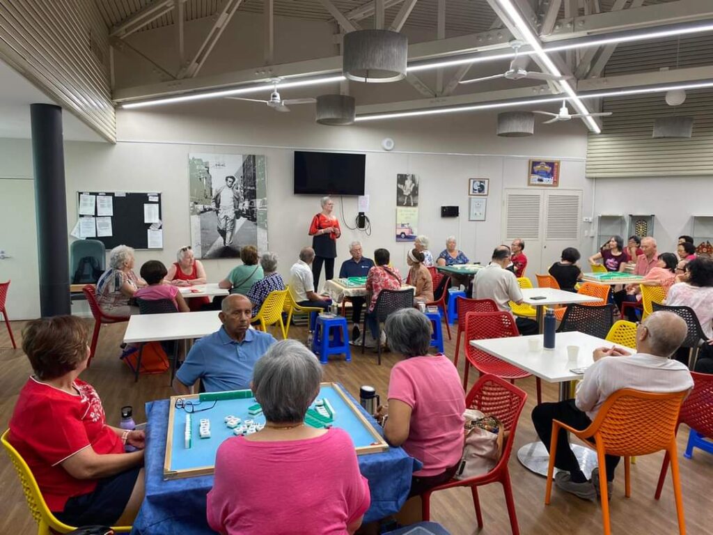 senior people sitting at tables with Monika standing and speaking