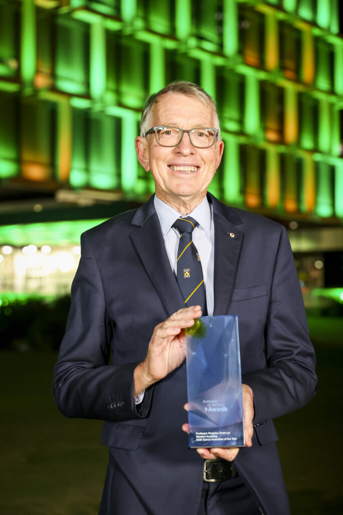 Kingsley Dixon smiles to camera holding trophy