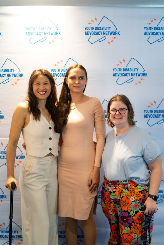 three people standing in front of media wall and smiling