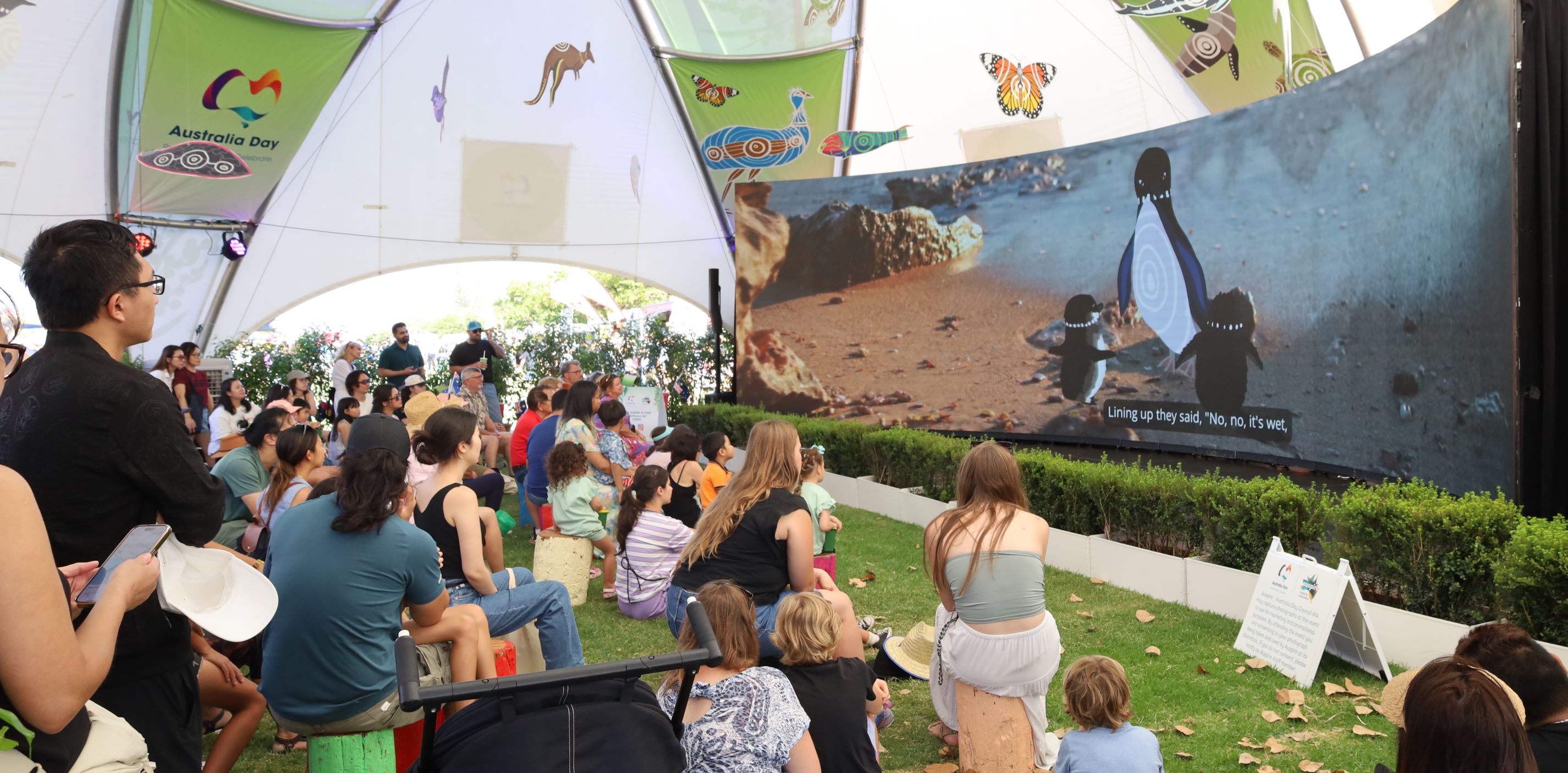 wide screen with illustrated penguins with audience watching inside dome marquee