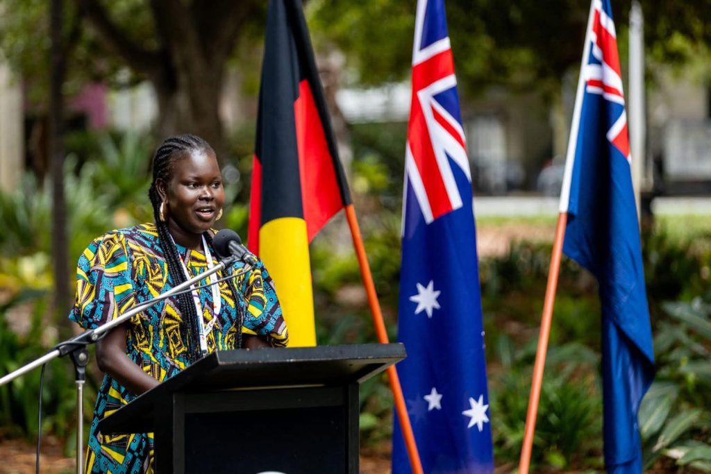 Lueth Garang speaking with Australian and Aboriginal flags behind