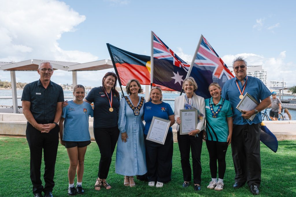 group of people standing on grass with certificates and medals, smiling to camera, Australian and Aboriginal flags in background