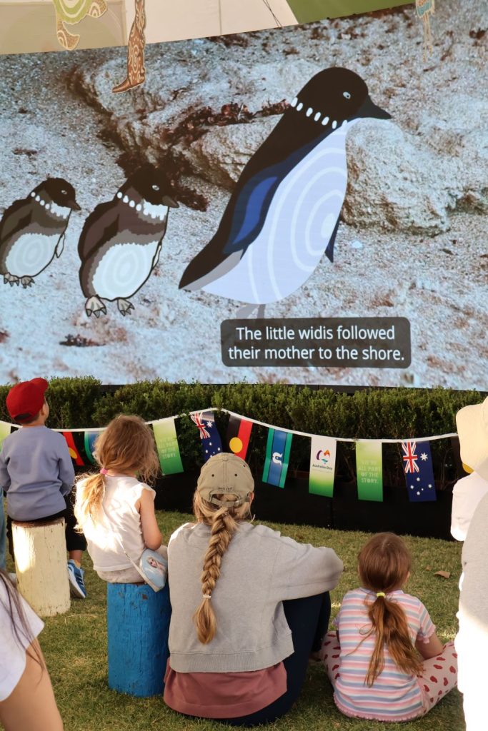 woman and two children watching animated penguins on screen