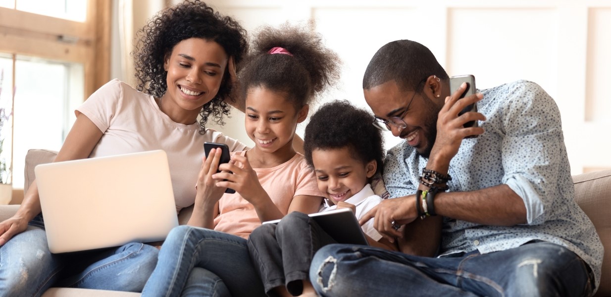 family sitting on a sofa using laptops and smartphones