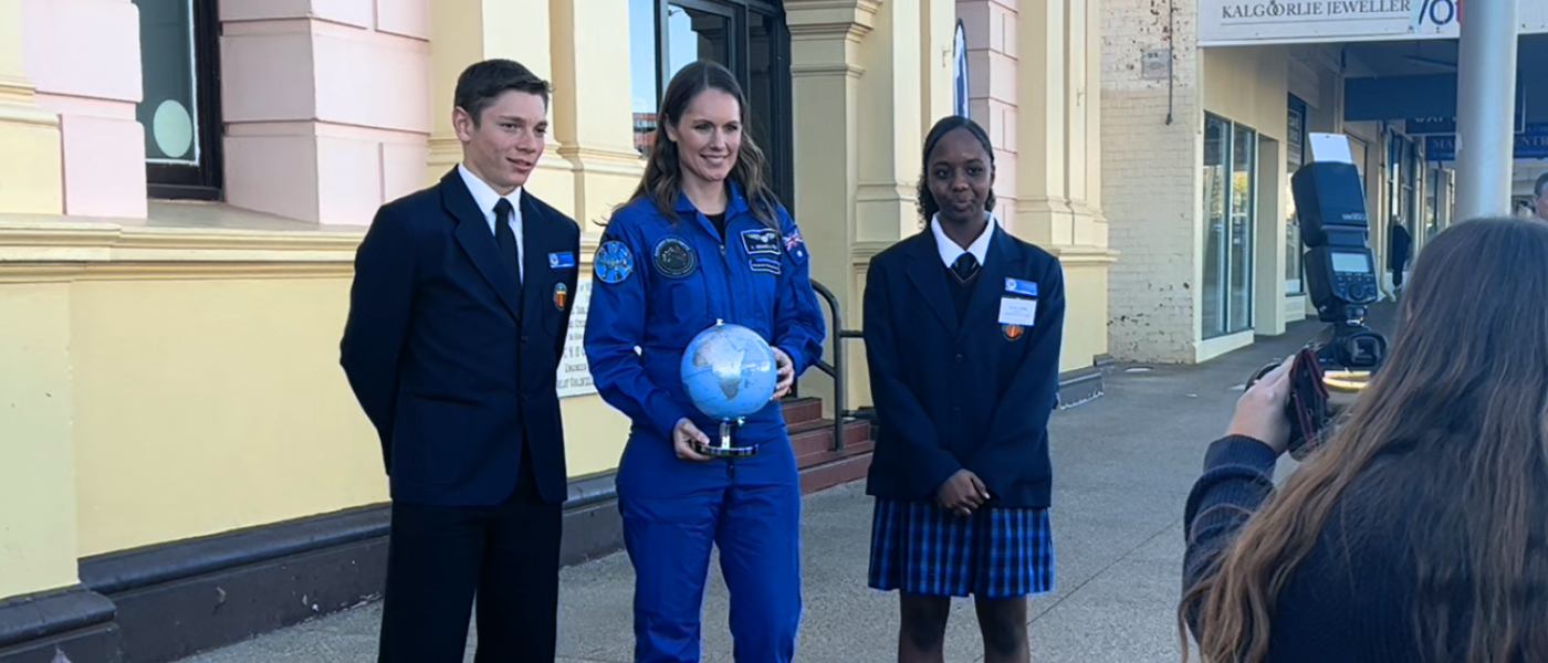 Katherine Bennelll-Pegg holding globe between two students and smiling to camera